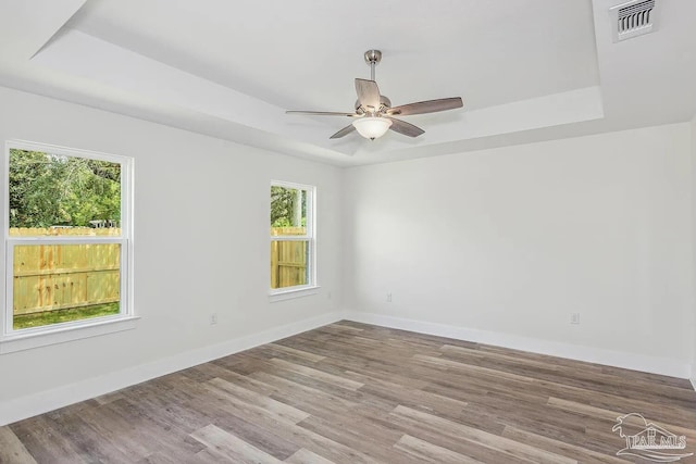 unfurnished room with light hardwood / wood-style flooring, ceiling fan, and a raised ceiling