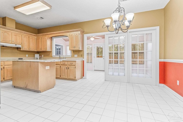 kitchen with light tile patterned flooring, ceiling fan with notable chandelier, a center island, decorative light fixtures, and sink