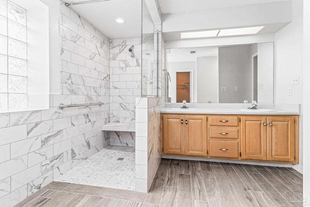 bathroom with a skylight, tiled shower, double sink vanity, and hardwood / wood-style floors