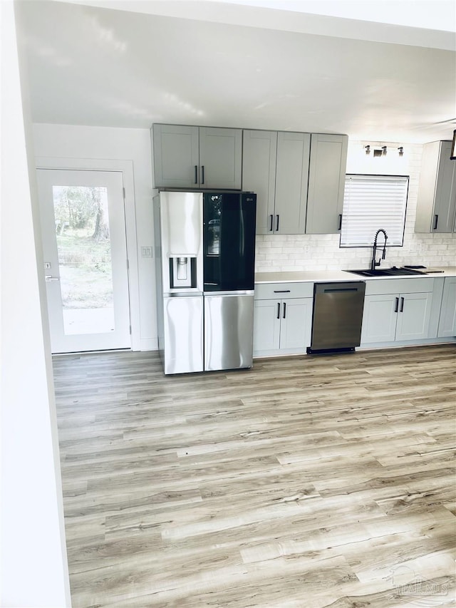 kitchen with dishwashing machine, sink, backsplash, light hardwood / wood-style floors, and stainless steel fridge with ice dispenser