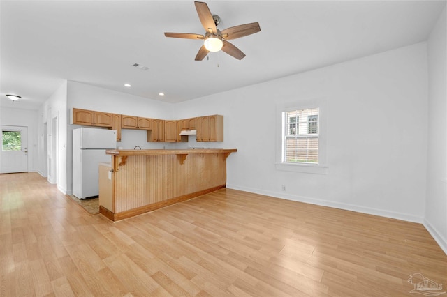 kitchen with light wood-type flooring, a breakfast bar, kitchen peninsula, and white fridge