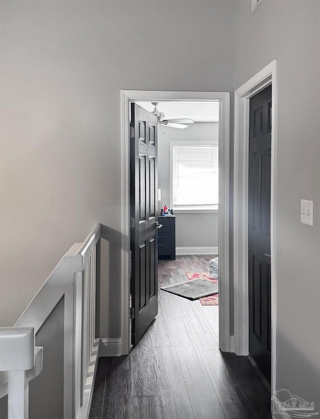 corridor featuring an upstairs landing, dark wood-type flooring, and baseboards