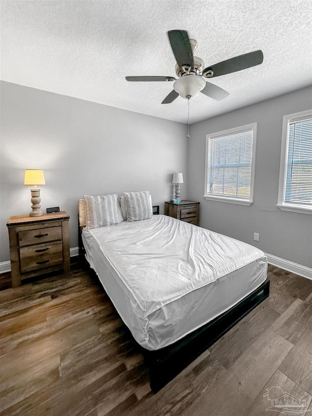 bedroom with baseboards, multiple windows, a textured ceiling, and wood finished floors