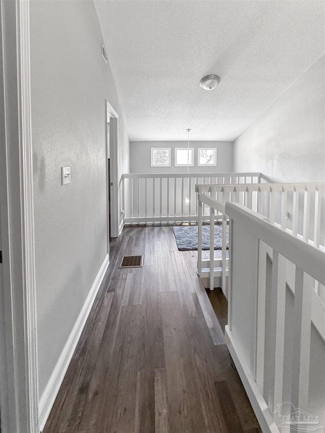 hall featuring visible vents, a textured ceiling, baseboards, and dark wood finished floors