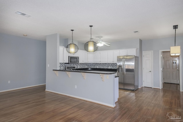 kitchen featuring backsplash, kitchen peninsula, a breakfast bar area, white cabinets, and appliances with stainless steel finishes