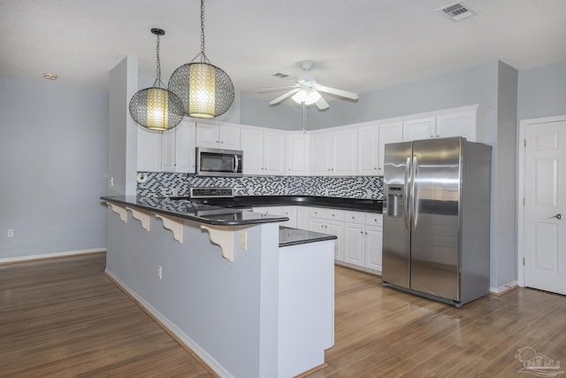 kitchen with white cabinets, a kitchen breakfast bar, hanging light fixtures, appliances with stainless steel finishes, and kitchen peninsula