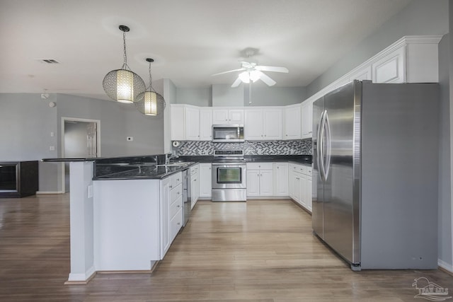 kitchen with kitchen peninsula, appliances with stainless steel finishes, tasteful backsplash, decorative light fixtures, and white cabinetry