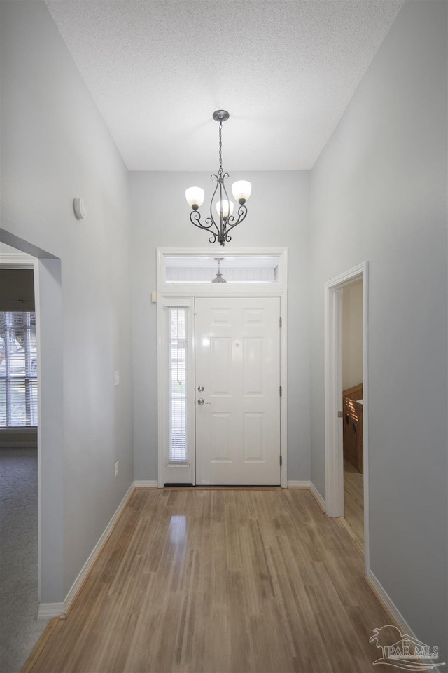 entrance foyer with wood-type flooring, a textured ceiling, a towering ceiling, and a chandelier