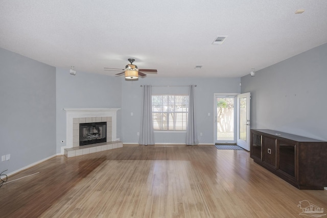 unfurnished living room with ceiling fan, light wood-type flooring, a textured ceiling, and a tile fireplace