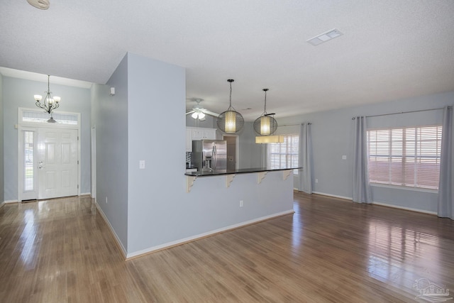 kitchen featuring a breakfast bar, stainless steel fridge, white cabinetry, and pendant lighting