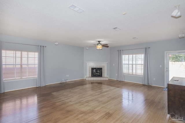 unfurnished living room with light hardwood / wood-style floors, ceiling fan, and a tiled fireplace