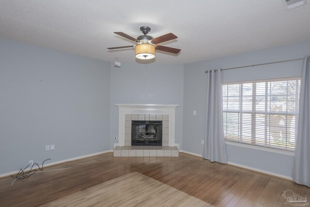 unfurnished living room featuring a tile fireplace, ceiling fan, wood-type flooring, and a textured ceiling