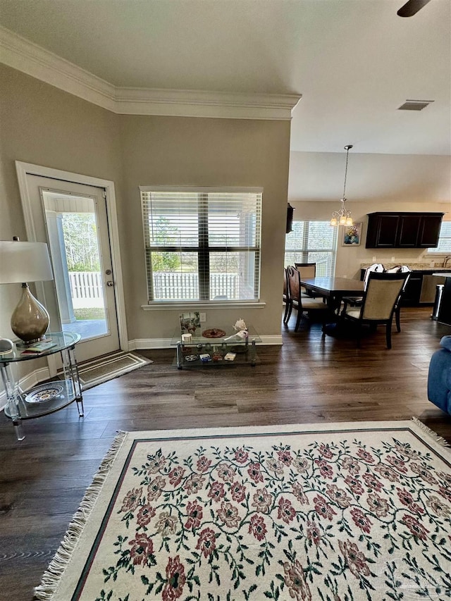 living room with dark wood-type flooring, crown molding, and an inviting chandelier