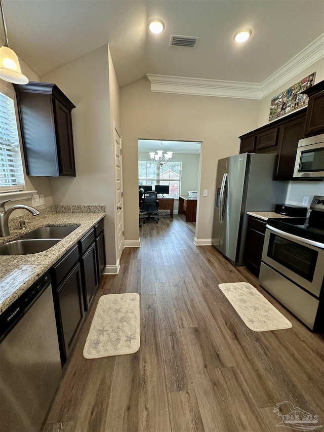 kitchen with dark brown cabinets, stainless steel appliances, light stone counters, decorative light fixtures, and sink