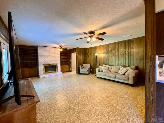 unfurnished living room featuring built in shelves, ceiling fan, wood walls, a textured ceiling, and a fireplace