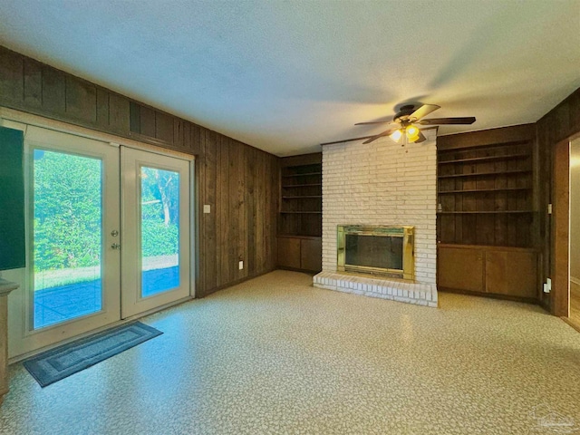 unfurnished living room with a fireplace, a textured ceiling, built in features, and wooden walls