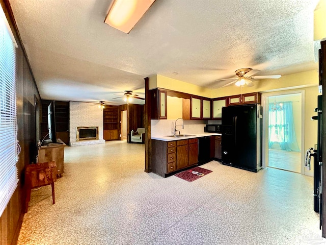 kitchen featuring a brick fireplace, a textured ceiling, ceiling fan, sink, and black appliances