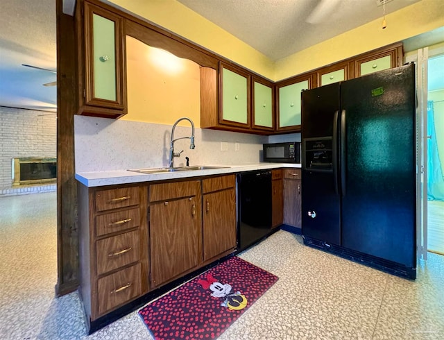 kitchen featuring black appliances, a textured ceiling, sink, and a brick fireplace