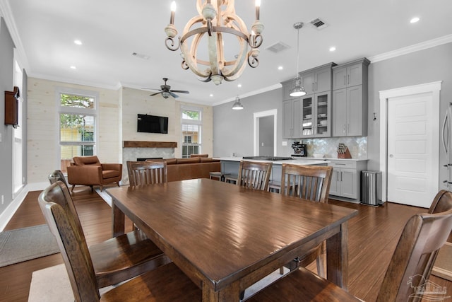 dining area featuring a ceiling fan, dark wood-style floors, a chandelier, a fireplace, and ornamental molding