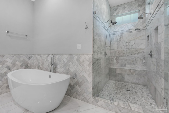 bathroom featuring a stall shower, a freestanding bath, tile walls, marble finish flooring, and wainscoting