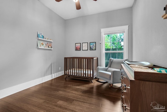 bedroom with dark wood-type flooring, a crib, and ceiling fan