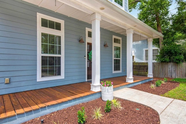 view of exterior entry with a porch and fence
