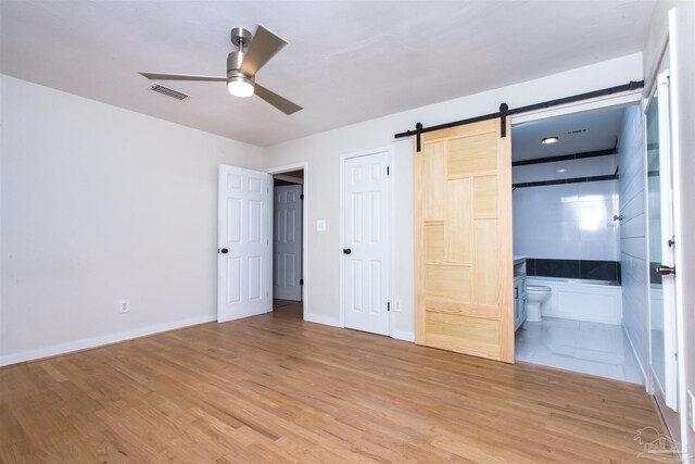7402 Viewcrest Dr, Pensacola, FL 32504 - unfurnished bedroom featuring a barn door, light wood-style floors, connected bathroom, baseboards, and ceiling fan