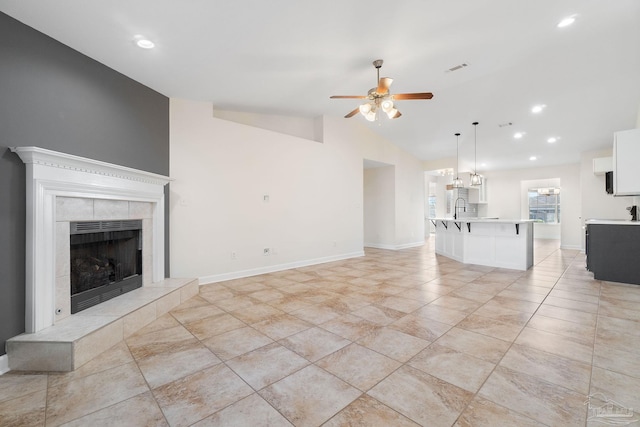 unfurnished living room featuring a tiled fireplace, ceiling fan, sink, and lofted ceiling