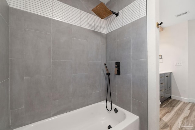 bathroom with hardwood / wood-style flooring, vanity, and tiled shower / bath combo