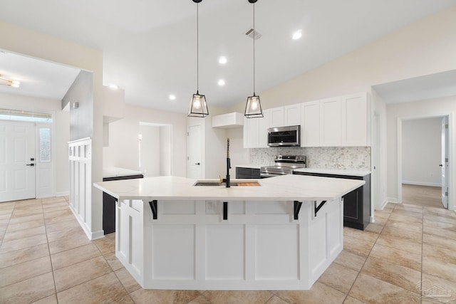 kitchen with tasteful backsplash, stainless steel appliances, vaulted ceiling, a center island with sink, and white cabinetry