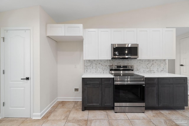 kitchen with white cabinets, vaulted ceiling, decorative backsplash, light tile patterned floors, and appliances with stainless steel finishes