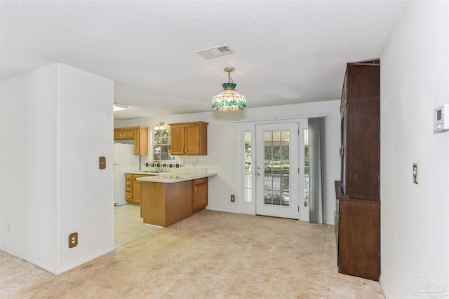 939 Avalon Blvd, Milton, FL 32583 - kitchen featuring a peninsula, light countertops, brown cabinets, freestanding refrigerator, and hanging light fixtures