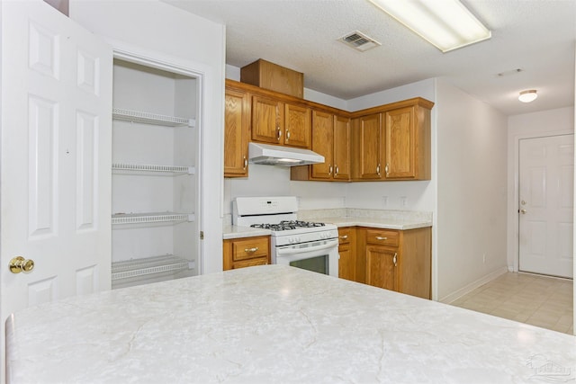 939 Avalon Blvd, Milton, FL 32583 - kitchen with white range with gas stovetop, under cabinet range hood, light countertops, brown cabinets, and light floors
