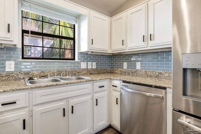 kitchen with light stone counters, stainless steel appliances, a sink, white cabinetry, and decorative backsplash