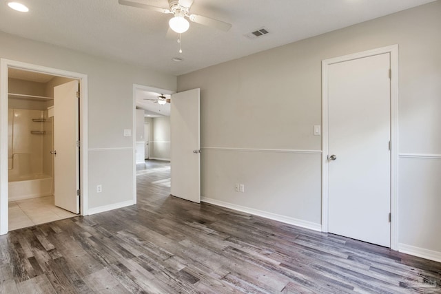 unfurnished bedroom featuring visible vents, ensuite bath, baseboards, and wood finished floors