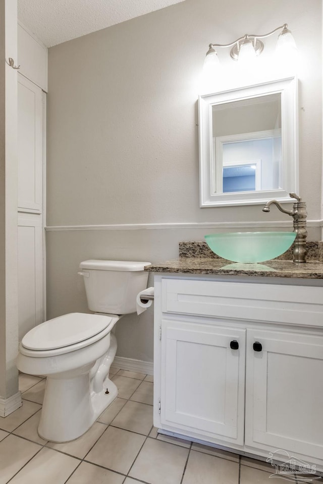 half bathroom featuring baseboards, toilet, tile patterned flooring, a textured ceiling, and vanity