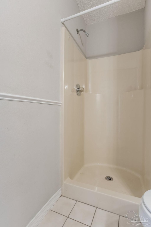 bathroom with a textured ceiling, toilet, baseboards, a shower stall, and tile patterned floors