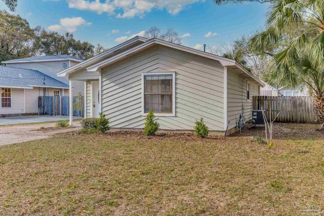 view of side of home with central AC unit, fence, and a yard