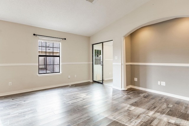 unfurnished room featuring lofted ceiling, a textured ceiling, baseboards, and wood finished floors