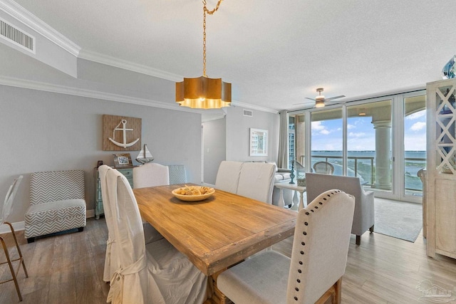 dining room with a water view, wood-type flooring, crown molding, a textured ceiling, and a wall of windows