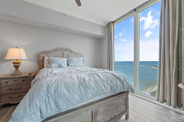 bedroom featuring ceiling fan, crown molding, hardwood / wood-style floors, a textured ceiling, and a water view