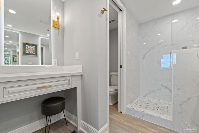 bathroom with a tile shower, vanity, wood-type flooring, and toilet