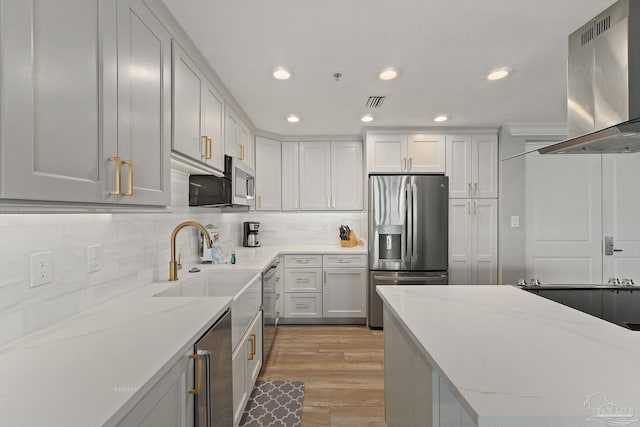 kitchen featuring light stone countertops, wall chimney exhaust hood, stainless steel appliances, light hardwood / wood-style floors, and white cabinets