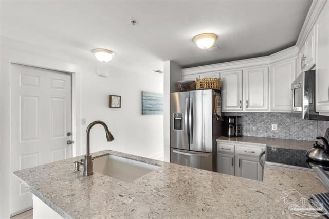 kitchen featuring a sink, stainless steel appliances, decorative backsplash, and light stone counters