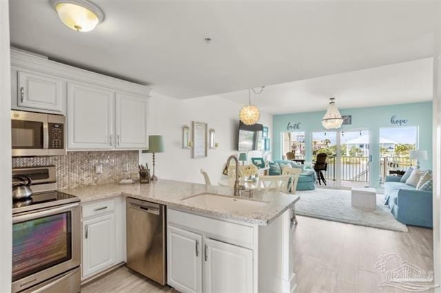 kitchen featuring a peninsula, appliances with stainless steel finishes, open floor plan, and a sink