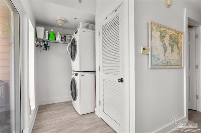 clothes washing area with baseboards, light wood finished floors, and stacked washing maching and dryer