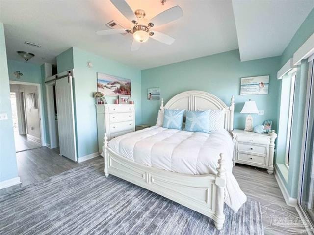 bedroom featuring baseboards, multiple windows, a barn door, and wood finished floors