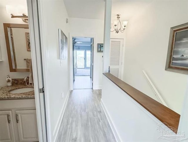 corridor featuring a sink, a notable chandelier, light wood-type flooring, and baseboards