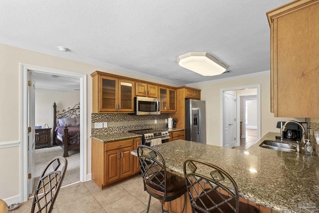 4621 Riley Rd, Milton, FL 32583 - kitchen featuring stainless steel appliances, brown cabinetry, ornamental molding, a peninsula, and glass insert cabinets