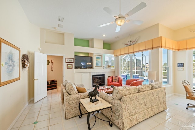 tiled living room featuring a towering ceiling, ceiling fan, and a tiled fireplace